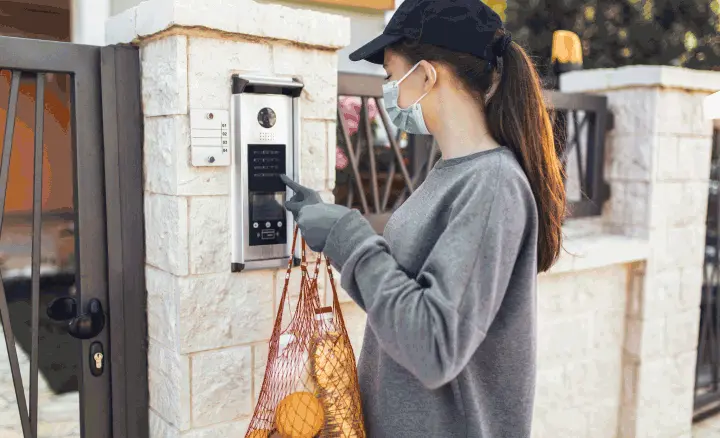 Woman using the intercom outside a gated property to call resident and parents and child freely enjoying the outdoors in a beautiful residential compound